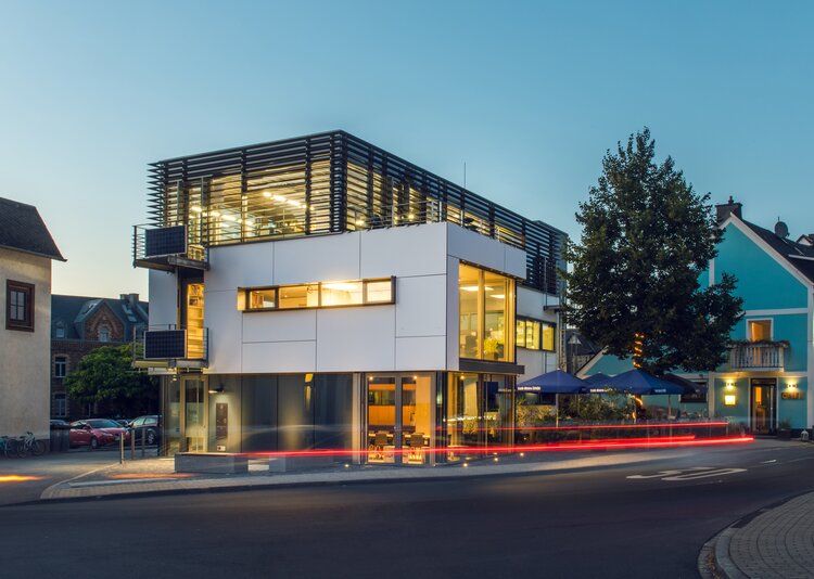 Modernes energieeffizientes Bürogebäude in Koblenz bei Dämmerung mit beleuchteter Fassade und Lichtspuren auf der Straße.